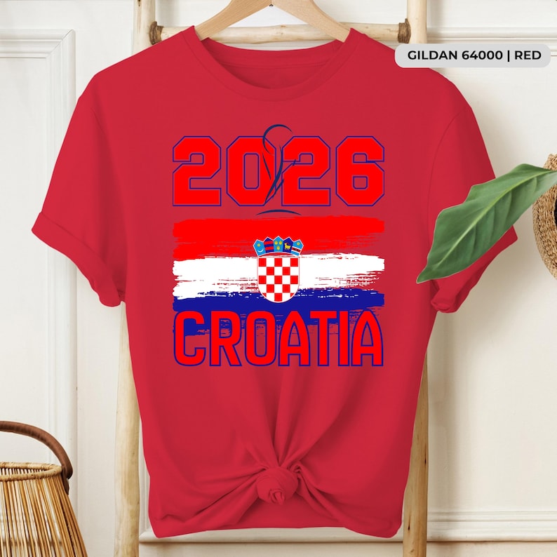 May include: Red t-shirt featuring the text "2026 CROATIA" in blue, with a Croatian flag design. The shirt is made of red fabric and has a crew neck. The text "GILDAN 64000 | RED" is printed on the upper right.