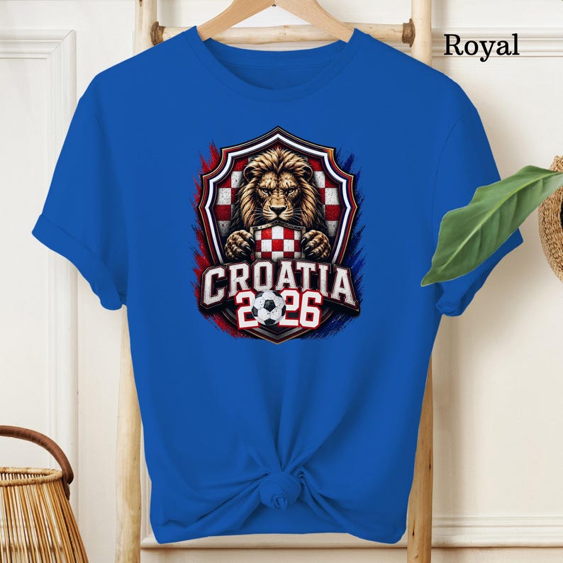 May include: Royal blue t-shirt featuring a graphic of a lion holding a Croatian flag, with the text "CROATIA 2026" and a soccer ball. The design is set within a shield shape with red, white, and blue accents.