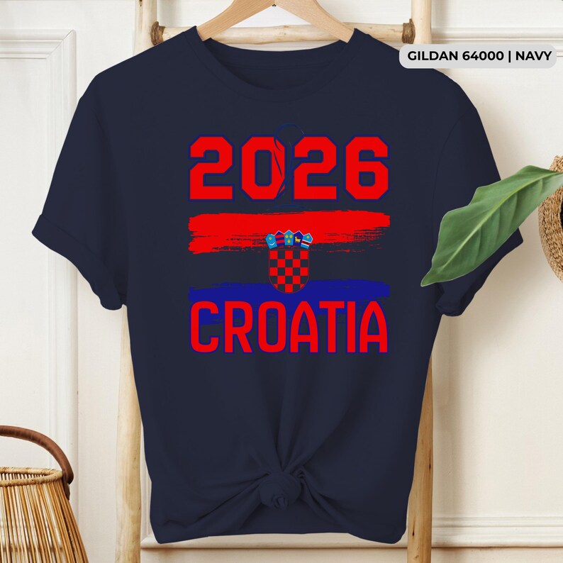 May include: Navy blue t-shirt with the text "2026 CROATIA" in red, featuring a red and blue brushstroke design and a Croatian coat of arms. The shirt is a Gildan 64000 in navy.