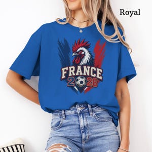 May include: Royal blue t-shirt featuring a graphic of a rooster, the French flag colors, and the text "FRANCE 2026" with a soccer ball. The shirt is a short-sleeved crew neck.