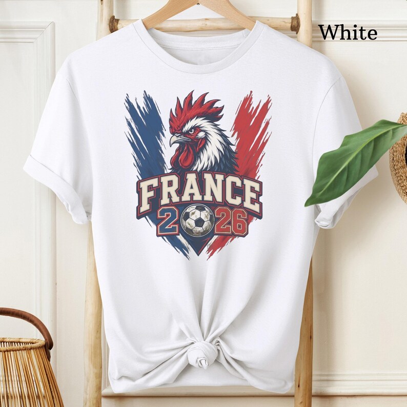May include: White t-shirt featuring a graphic of a rooster with the French flag colors and the text "FRANCE 2026" and a soccer ball. The shirt is tied at the waist.