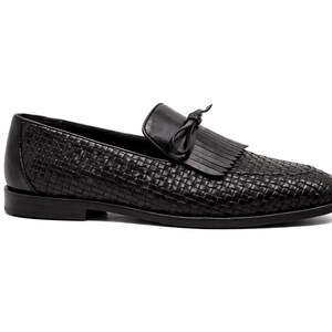 May include: Black woven leather loafer with a tassel detail. The shoe features a rounded toe and a low heel. The upper is made of a woven leather material, and the shoe has a classic, timeless design.