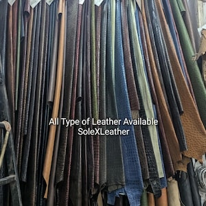 May include: A collection of hanging leather hides in various colors and textures, including embossed crocodile and ostrich patterns. The text "All Type of Leather Available SoleXLeather" is printed across the center of the display.