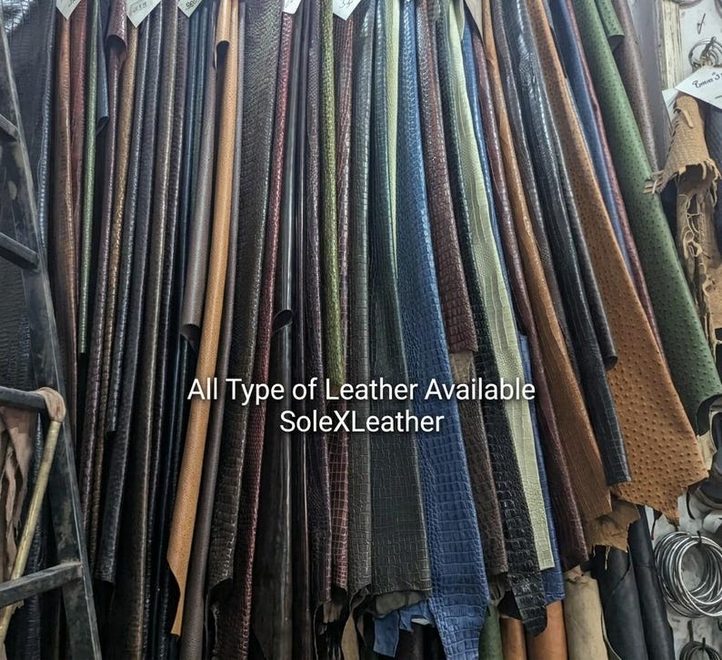 May include: A collection of hanging leather hides in various colors and textures, including embossed crocodile and ostrich patterns. The text "All Type of Leather Available SoleXLeather" is printed across the center of the display.