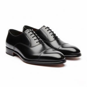Könnte beinhalten: Ein Paar schwarze Oxford-Schuhe aus Leder mit glänzender Oberfläche. Die Schuhe haben ein klassisches Cap-Toe-Design, schwarze Schnürsenkel und einen niedrigen Absatz. Die Schuhe werden vor weißem Hintergrund präsentiert.