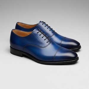 May include: A pair of blue leather dress shoes with black laces and soles. The shoes have a classic Oxford design with a cap toe and a polished finish. The shoes are displayed on a neutral background.