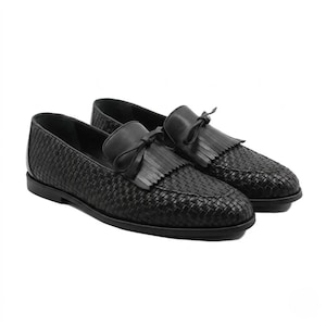 A pair of premium handmade black woven leather loafers for men featuring a traditional kiltie fringe and tassel tie. The shoes showcase a detailed hand-braided texture (intrecciato) on the body and a smooth leather tongue, set against a clean white background to emphasize the luxury craftsmanship.