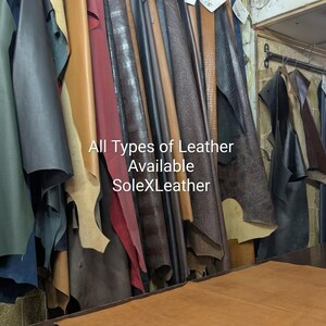 May include: A collection of various leather hides in shades of green, black, tan, red, and brown hanging from a rack. The text All Types of Leather Available SoleXLeather is printed in white over the center of the hanging leather pieces.
