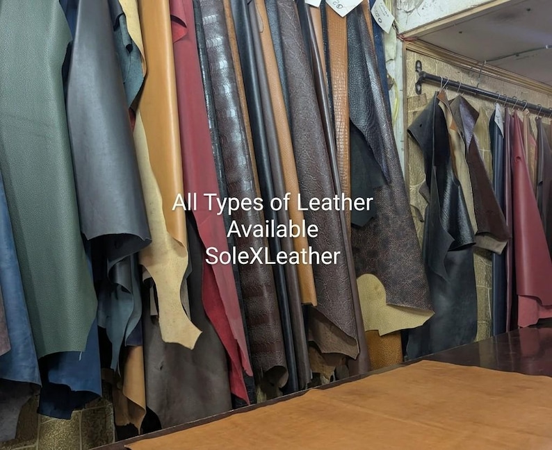 May include: A collection of various leather hides in shades of green, black, tan, red, and brown hanging from a rack. The text All Types of Leather Available SoleXLeather is printed in white over the center of the hanging leather pieces.