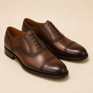May include: A pair of dark brown leather oxford shoes featuring a cap toe design with decorative brogue detailing along the seams and eyelet panels. The shoes have thin dark brown laces and a low stacked heel with a smooth polished finish.