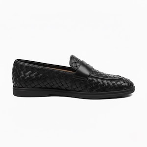Könnte beinhalten: Schwarzer Leder-Loafer mit gewebtem Design. Der Schuh hat eine runde Spitze, einen Riemen über dem Oberteil und eine flache, feste Sohle. Ein klassischer Stil.
