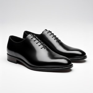 Könnte beinhalten: Ein Paar schwarze Oxford-Schuhe aus Leder mit polierter Oberfläche, ausgestattet mit einem geschlossenen Schnürsystem, abgerundeten Zehenkappen und dünnen schwarzen Schnürsenkeln. Die Schuhe haben einen niedrigen Absatz und ein glattes Design.