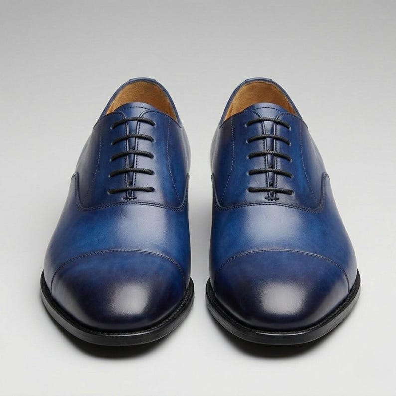 May include: A pair of blue leather Oxford shoes with black laces. The shoes have a classic design with a rounded toe and a dark blue gradient. The soles are black.
