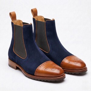 Puede incluir: Un par de botines Chelsea de ante azul con detalles en cuero marrón. Los botines tienen punteras de cuero marrón con perforaciones decorativas y una lengüeta. Las suelas son marrones.