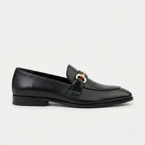 May include: A black leather loafer with a textured finish, featuring a gold-toned metal horsebit detail across the vamp. The shoe includes a green and red fabric stripe accent positioned behind the metal hardware and a low, flat heel.