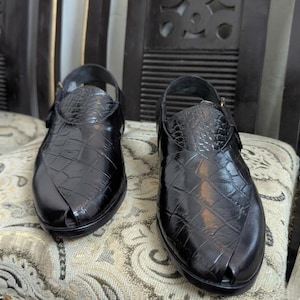May include: A pair of black sandals featuring a glossy finish and a textured crocodile-skin pattern. These open-toe sandals have a closed heel design with a buckled strap across the ankle area, showcasing a structured silhouette and a polished appearance.