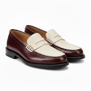 May include: A pair of two-tone loafers featuring a deep burgundy smooth leather heel and side panels paired with a textured cream-colored leather vamp. The shoes include a classic penny loafer strap across the top with visible stitching details.