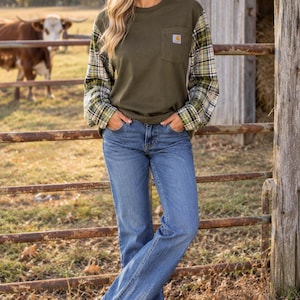 May include: An olive green long-sleeve shirt with a chest pocket and plaid sleeves in shades of green, white, and yellow, paired with blue denim jeans and brown leather boots. The shirt features a small rectangular logo patch on the pocket.