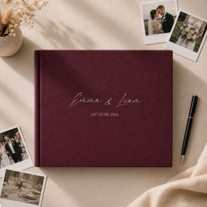 Może przedstawiać: Ciemnobordowy album fotograficzny pokryty tkaniną z białym, tłoczonym napisem "Emma & Liam" oraz datą "04TH JUNE 2026" wyśrodkowanymi na przedniej okładce. Album jest prostokątny i ma czystą, jednolitą powierzchnię.