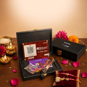 Op de afbeelding: Een zwarte rechthoekige geschenkdoos met een houtnerf-plaatje met een QR-code, de tekst "Shivax", "17, CIVIL LINES" en "SCAN ME". Binnenin zitten twee kralenarmbanden met rode en gouden accenten, plus een klein zakje met metalen onderdelen.
