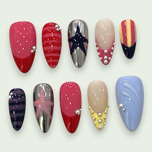 Puede incluir: Un conjunto de diez uñas postizas en forma de almendra con diseños variados, incluyendo tonos rojos y rosas, acabados en plata metálica con motivos de estrellas, patrones de rayas, bases nude con puntas amarillas o rosas y azul.