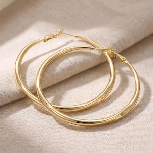 Può includere: Un paio di orecchini a cerchio color oro lucido caratterizzati da una superficie metallica liscia e arrotondata e da un meccanismo di chiusura a perno incernierato. Gli orecchini circolari presentano un design continuo e senza giunture.