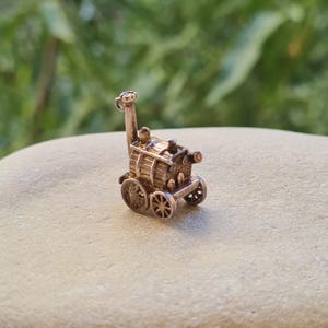 以下が含まれることがあります： ヴィンテージの蒸気機関車の形をした、ローズゴールド色の小さな金属製チャーム。高い煙突、水平なディテールが施された円筒形のボイラー、4つのスポークホイールが特徴です。上部には小さなループが付いています。
