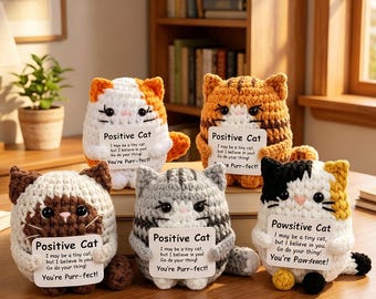 May include: Five crocheted cat plushies in various colours and patterns, each holding a small white sign. Four signs read Positive Cat with motivational text, and one sign reads Pawsitive Cat with similar text. The cats have black eyes and stitched details.