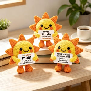 Op de afbeelding: Drie gehaakte zonnefiguren met gele gezichten, oranje stralen en zwarte ogen. Elk figuur houdt een wit rechthoekig bordje vast. De bordjes bevatten de teksten: Happy Birthday You are truly SUN-sational, SUN-sational mom I LOVE YOU YOU ARE MY SUNSHINE!, en YOU ARE SUNSHINE IN HUMAN FORM Thank You For Sharing Your Sunshine.