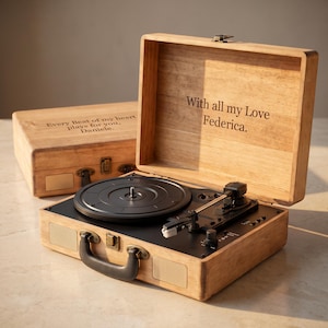 May include: A wooden suitcase-style record player with a black turntable and control panel. The interior lid is engraved with "With all my Love Federica." A matching wooden case behind it is engraved with "Every Beat of my heart plays for you, Daniele."