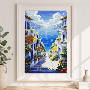 May include: Framed art print of a coastal village scene. White buildings with blue accents and orange tile roofs line a stepped street leading to a bright blue sea. Colourful flowers in pots adorn the balconies and steps.