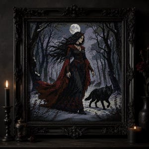 May include: A framed cross-stitch artwork depicting a person with long dark hair wearing a flowing black and red gown, walking through a snowy forest with a black wolf under a full moon. The piece is enclosed in an ornate black wooden frame.