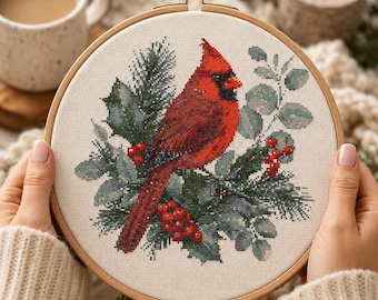May include: A round wooden embroidery hoop containing a cross-stitch pattern of a bright red cardinal bird perched among green pine needles, holly leaves, and small red berries on a light-colored fabric background with a metal tension screw.