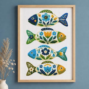 Può includere: Un ricamo a punto croce incorniciato che raffigura quattro pesci orizzontali disposti in una colonna verticale. Ogni pesce ha un corpo color crema decorato con intricati motivi floreali blu, gialli e verdi su uno sfondo di tessuto bianco.