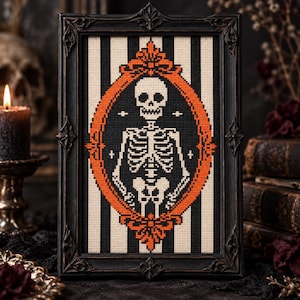 May include: A cross-stitch embroidery featuring a white skeleton centered within an orange oval frame, set against a black and white vertical striped background, all enclosed in a dark, ornate, rectangular wooden picture frame.