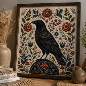 Könnte beinhalten: Eine gerahmte Kreuzstichstickerei mit einem zentralen schwarzen Raben, der auf einem dekorativen Halbkreis sitzt. Der Vogel ist von einem symmetrischen Blumenmuster mit roten, blauen und grünen botanischen Elementen auf cremefarbenem Stoff umgeben.