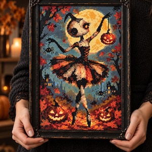 May include: A framed cross-stitch artwork depicting a stylized figure in a tutu holding a jack-o'-lantern against a large yellow moon. The scene includes autumn trees, two additional jack-o'-lanterns on the ground, and small spiders.