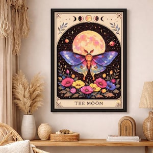 May include: Framed art print featuring a moth with blue and yellow wings, set against a full moon and starry night sky. The artwork includes colorful flowers and the text "THE MOON" at the bottom, framed in black.