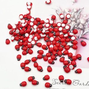 May include: A large collection of small, red ladybug-shaped embellishments with black spots and a black head. Each ladybug features a flat, white adhesive backing, making them suitable for various craft projects. The ladybugs are scattered across the surface.