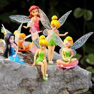 K&ouml;nnte beinhalten: Eine Sammlung von Feenfiguren mit durchscheinenden Fl&uuml;geln. Die Feen sind in verschiedenen Posen dargestellt und tragen Kleider in Gr&uuml;n, Rosa und Blau. Einige haben blondes Haar, andere schwarzes oder rotes Haar. Sie sind auf einem grauen Felsen angeordnet.