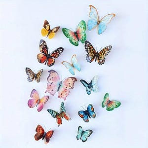 以下が含まれることがあります： 青、緑、オレンジ、黄色、ピンクの色合いを含む、さまざまなサイズと色の15個の装飾的な蝶の切り抜きコレクション。各蝶は、繊細なディテールと細い触角を備えた複雑な羽の模様が特徴です。