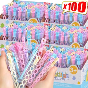May include: A bulk set of 100 colorful plastic bubble wands in a cardboard display box. Each wand features a clear tube filled with bubble solution and a decorative cap in shapes like crowns, stars, and animal paws in pastel pink, blue, and yellow.