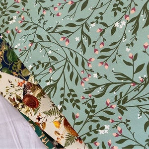 May include: Three different fabric swatches with floral patterns. The top swatch is a light blue background with dark green leaves and pink and white flowers. The middle swatch is a cream background with brown mushrooms and green leaves. The bottom swatch is a dark blue background with white and brown flowers and leaves.