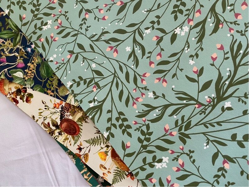 May include: Three different fabric swatches with floral patterns. The top swatch is a light blue background with dark green leaves and pink and white flowers. The middle swatch is a cream background with brown mushrooms and green leaves. The bottom swatch is a dark blue background with white and brown flowers and leaves.