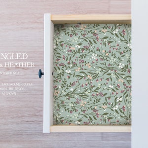 May include: A drawer liner with a sage green background and a floral pattern featuring white, pink, and burgundy flowers. The text "TANGLED SAGE & HEATHER STANDARD SCALE CUSTOMIZE BACKGROUND COLOUR OR ORDER THE DESIGN AS SHOWN" is printed on the drawer liner.