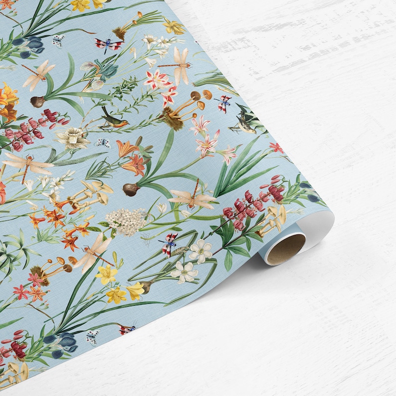 May include: A roll of wallpaper featuring a detailed botanical design. The pattern includes various flowers, dragonflies, and birds in shades of red, orange, yellow, and white against a light blue background. The paper is rolled up, showing the pattern's repeating nature.