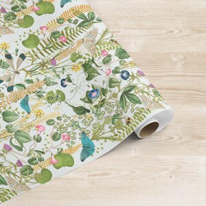 May include: A white wrapping paper with a repeating pattern of green leaves, yellow flowers, blue butterflies, and small insects. The paper is rolled up and the end is visible.