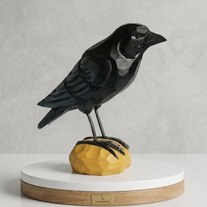 May include: A carved black raven sculpture perched on a yellow rock. The bird is detailed with carved feathers and stands on a white and wood-tone base. The sculpture is a decorative item.