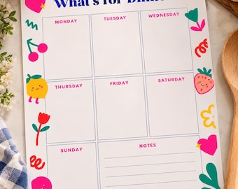 以下が含まれることがあります： 青い文字で「What's for Dinner?」と書かれた週間の献立表。月曜日から日曜日までの7つの枠とメモ欄がある。枠の周りには、果物、ハート、花などのカラフルなイラストが描かれている。