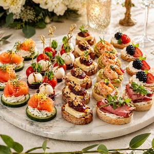 Puede incluir: Una fuente de mármol exhibe una variedad de aperitivos. Incluyen rodajas de pepino con salmón y queso crema, brochetas de tomate y mozzarella, y pan tostado con diferentes ingredientes como brie, camarones y rosbif. Adornado con hierbas y bayas.